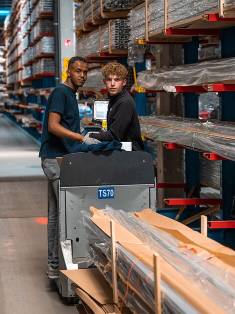 Two Reynaers co-workers transporting aluminium profiles in the warehouse.